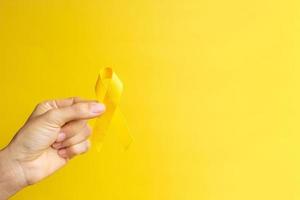 mano que muestra una cinta amarilla sobre fondo amarillo para apoyar a las personas que viven y están enfermas. día de prevención del suicidio de septiembre, mes de concientización sobre el cáncer infantil y concepto del día mundial contra el cáncer foto
