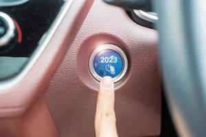 Finger press a car ignition button with 2023 START text inside  automobile. New Year New You, forecast, resolution, motivation, change, goal, vision, innovation and planning concept photo