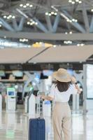 Young woman hand holding luggage handle before checking flight time in airport, Transport, insurance, travel and vacation concepts photo