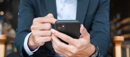 young Businessman in suit holding and using smartphone for sms messages, man typing touchscreen mobile phone in office or cafe. business, lifestyle, technology and Social media network concept photo