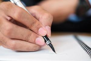 Businessman in suit writing something on notebook in office or cafe, hand of man holding pen with signature on paper report. business concepts photo