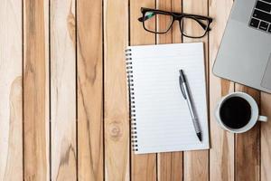 Top view Office desk with pen, computer laptop, blank notebook, plant pot and coffee cup on wood table background. workspace or home office with copy space for text concept photo