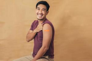 Asian man showing shoulders after getting a vaccine. Happy man showing arm with band-aids on after vaccine injection. photo