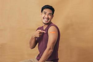 Asian man showing shoulders after getting a vaccine. Happy man showing arm with band-aids on after vaccine injection. photo