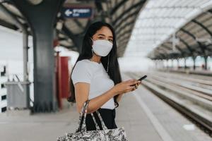 Asian woman wearing protective mask standing and waiting for sky train. woman wearing surgical protective mask in a public transportation. New normal concept.
