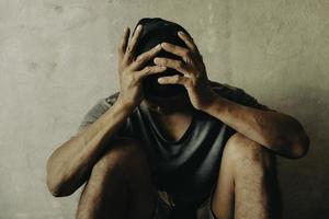 A drug addicted homeless man sitting alone and depressed in an abandoned house feeling anxious and lonely. photo