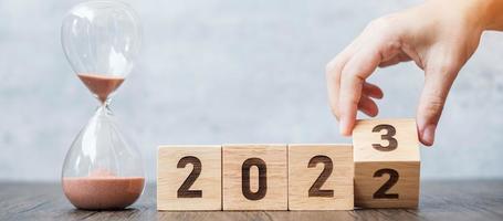 hand flip block 2022 to 2023 text with hourglass on table. Resolution, time, plan, goal, motivation, reboot, countdown  and New Year holiday concepts photo
