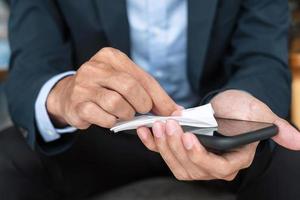 Businessman in suit cleaning smartphone by wet wipes tissue and alcohol disinfectant at office or cafe, protection coronavirus. infection. Clean surface and New Normal concept photo