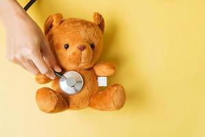 hand holding Stethoscope on Bear doll for supporting kid living and illness. September Childhood Cancer Awareness month, healthcare and life insurance concept photo