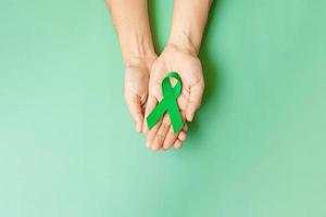 mano sosteniendo una cinta verde para apoyar a las personas que viven y están enfermas. concepto del mes de concientización sobre el hígado, las vesículas biliares, el cáncer de riñón y el linfoma foto