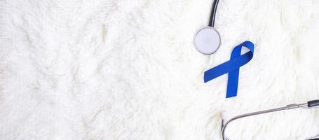 marzo mes de concientización sobre el cáncer colorrectal, cinta azul oscuro con estetoscopio sobre fondo blanco para apoyar a las personas que viven y están enfermas. concepto de salud, esperanza y día mundial contra el cáncer foto