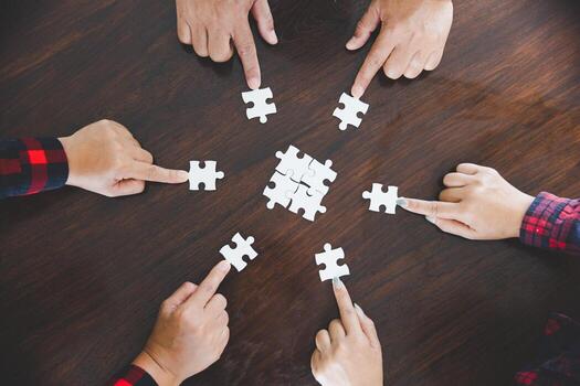 people helping in assembling puzzle, cooperation in decision making, team support in solving problems and corporate group teamwork concept, close up view of hands connecting pieces photo