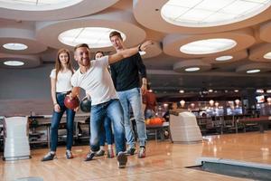 Confident in his own strenght. Young cheerful friends have fun in bowling club at their weekends photo