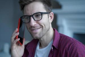 joven alemán sonriente con gafas usando teléfono móvil y hablando con un amigo foto