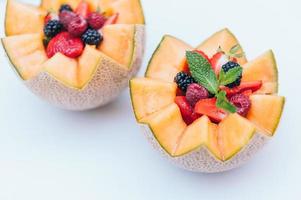 diseño de alimentos y concepto de nutrición saludable. Deliciosa fresca frambuesa, fresa y mora con menta en melón tallado. melón con fruta sobre fondo blanco. foto