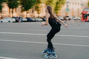 estilo de vida activo y concepto de hobby. una joven deportiva hace deporte al aire libre paseos en patines vestidos con ropa deportiva disfruta de poses de actividades físicas en un lugar urbano en la carretera. patinaje sobre ruedas. foto