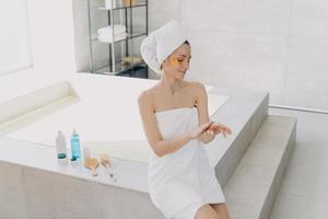 Girl applies eye patches and hand cream. Attractive caucasian woman wrapped in towel at spa resort. photo