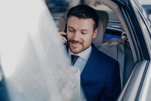el hombre de negocios viaja en un auto negro en el asiento del pasajero y habla por teléfono celular foto