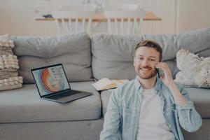 Young smiling male freelance worker calling his client to notify him about finishing project photo