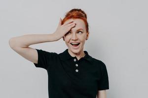 Happy young redhead woman with opened mouth touching her forehead with hand photo