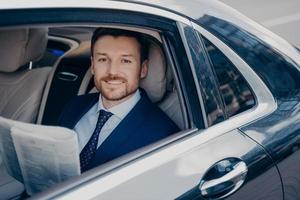 joven empresario con estilo lee el periódico en el asiento trasero del coche foto