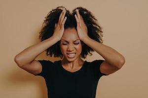 Chica afroamericana de pánico sorprendida vestida con una camiseta negra cogida de la mano en la cabeza foto
