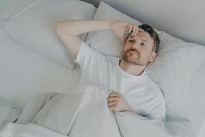 Young tired bearded man lying on bed with open eyes photo