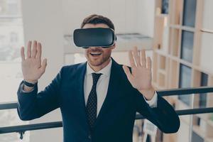 Smiling office worker in suit in 3d goggles enjoying cyberpace experience with raised arms photo