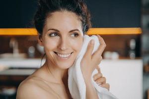 rutina de belleza e higiene nocturna. la mujer feliz caucásica se está limpiando la cara con una toalla después del lavado. foto