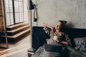 Happy relaxed positive young girl freelancer drinking coffee before to start working remotely at home photo