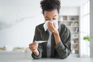 Young hispanic woman is measuring temperature with thermometer, sneezing and blowing running nose. photo