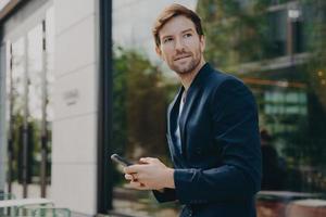 Pensive businessman holds cellular sends text messages dressed formally photo