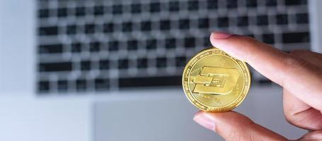 mano de hombre de negocios sosteniendo una moneda de criptomoneda golden dash sobre una computadora portátil con teclado, crypto es dinero digital dentro de la red blockchain foto