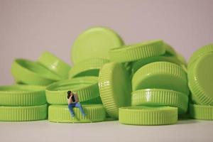 Man figure siting on plastic cap. Recycle material concept. photo