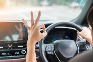 mujer mostrando el signo de ok durante la conducción de un automóvil en la carretera, controlando a mano el volante en un automóvil eléctrico moderno. conceptos de transporte de viaje, viaje y seguridad foto