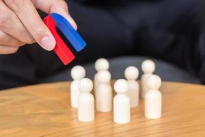 Businessman hand holding magnet and pulling man wooden figure from the crowd employee. Business, Human resource management, Recruitment, Teamwork, strategy, toxic people and leadership Concepts photo