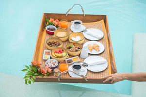 con una bandeja de desayuno flotante en un hotel de lujo con piscina, una chica disfruta en un resort tropical. viajes de verano relajantes y exóticos, vacaciones, vacaciones y tropicales foto