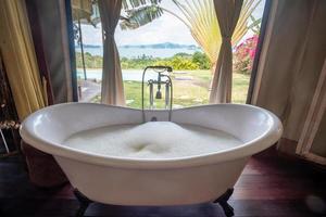 bathtub with foam bubbles in tropical luxury resort against beautiful ocean background. Spa and relaxation concepts photo