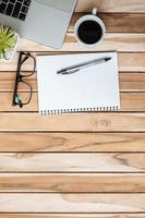 Top view Office desk with pen, computer laptop, blank notebook, plant pot and coffee cup on wood table background. workspace or home office with copy space for text concept photo