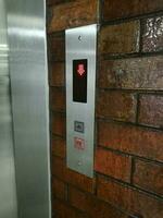 Elevator's keypad has a red light on the down button and a down arrow symbol. Keypad is mounted next to the elevator on a brown wall. photo