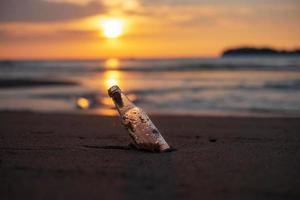 basura de botellas de vidrio en la playa contra el fondo de la puesta de sol. concepto de ecología, medio ambiente, contaminación y problema ecológico foto