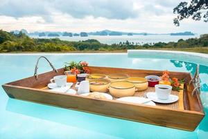 Floating Breakfast tray in swimming pool at luxury hotel or tropical resort villa, fruits, croissant, coffee, and orange juice. Exotic summer, relaxation, tropical travel and vacation concept photo