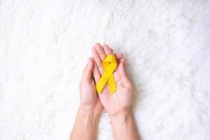 mano sosteniendo una cinta amarilla sobre fondo blanco para apoyar a las personas que viven y están enfermas. día de prevención del suicidio de septiembre, mes de concientización sobre el cáncer infantil y concepto del día mundial contra el cáncer foto