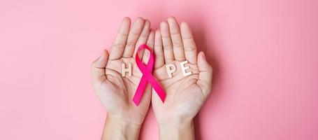 octubre mes de concientización sobre el cáncer de mama, mano de mujer adulta sosteniendo una cinta rosa sobre fondo rosa para apoyar a las personas que viven y están enfermas. concepto del día internacional de la mujer, la madre y el día mundial del cáncer foto