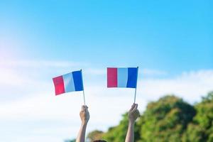 mano que sostiene la bandera de Francia sobre fondo de cielo azul. fiesta del día nacional francés, día de la bastilla y conceptos de celebración feliz foto