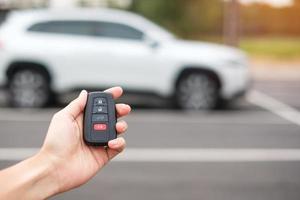 Hand holding car remote control, smart key to lock or unlock doors of white car. Safety, travel and transportation concept photo