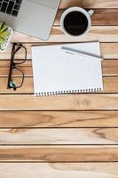 Top view Office desk with pen, computer laptop, blank notebook, plant pot and coffee cup on wood table background. workspace or home office with copy space for text concept photo