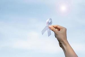 noviembre mes de concientización sobre el cáncer de pulmón, democracia y día internacional de la paz. mujer sosteniendo una cinta blanca en el fondo del cielo foto