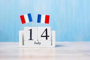 calendario de madera del 14 de julio con banderas de francia en miniatura. día nacional francés, día de la bastilla y conceptos de celebración feliz foto