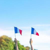 mano que sostiene la bandera de Francia sobre fondo de cielo azul. fiesta del día nacional francés, día de la bastilla y conceptos de celebración feliz foto